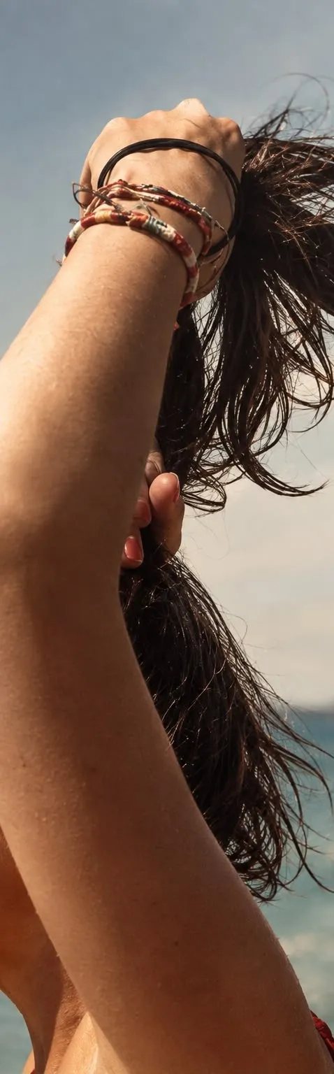 Brazo en alto sujetando el pelo mojado frente al mar